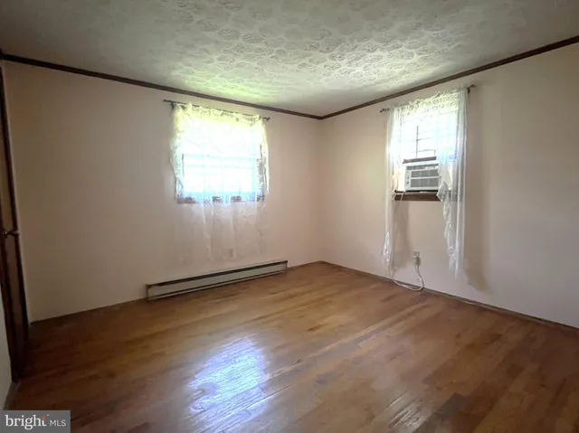 an empty room with wooden floor and windows with curtains