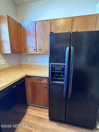 a view of a refrigerator in kitchen and an empty room in wooden floor