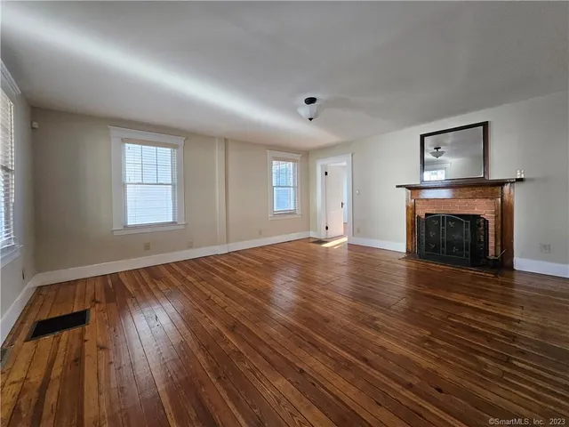 an empty room with wooden floor fireplace and windows