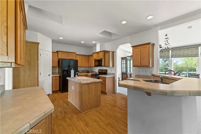 a kitchen with stainless steel appliances granite countertop a sink a stove a refrigerator cabinets and a dining table with wooden floor