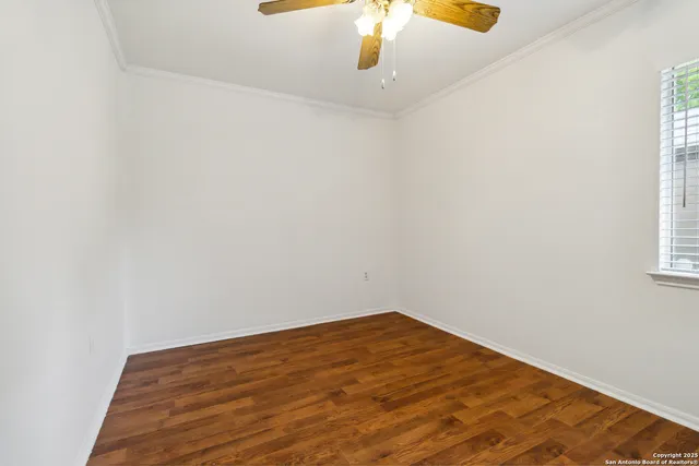 an empty room with a chandelier fan and wooden floor