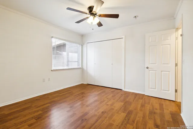 an empty room with wooden floor ceiling fan and windows