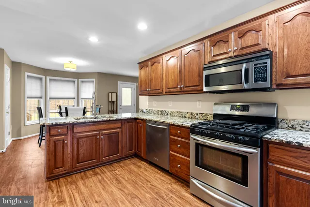 a kitchen with stainless steel appliances granite countertop wooden cabinets a stove a sink and a microwave