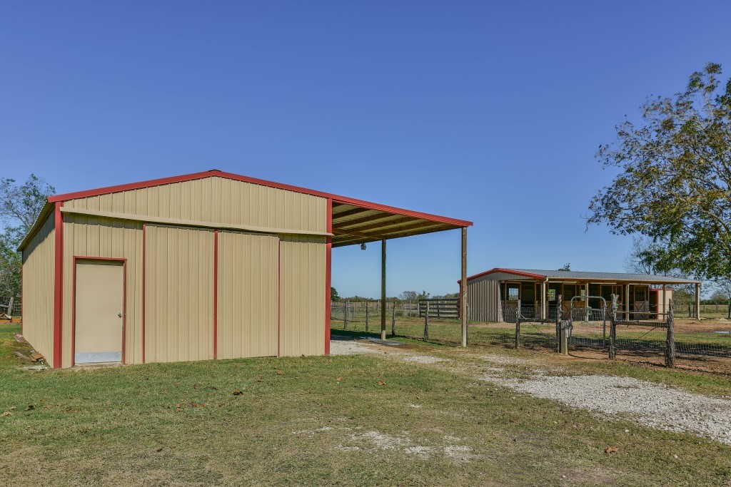 34366 Owens Road Hempstead, TX 77445 - Photo 42 of 46 Spacious metal equipment barn with a large covered lean-to and enclosed storage, offering flexible space for tractors, trailers, hay, livestock, or ranch equipment while overlooking the surrounding pasture.