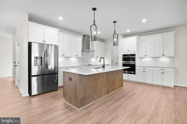 a large kitchen with stainless steel appliances a large counter top a stove a sink dishwasher and a refrigerator with wooden floors