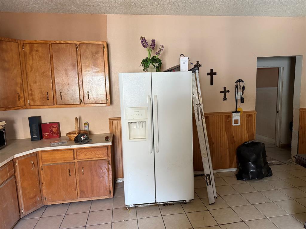 1530 Proctor Avenue Waco, TX 76708 - Photo 6 of 6 Kitchen area featuring wood-finish cabinetry, a white side-by-side refrigerator, light-toned countertops, tile flooring, and wood beadboard paneling
