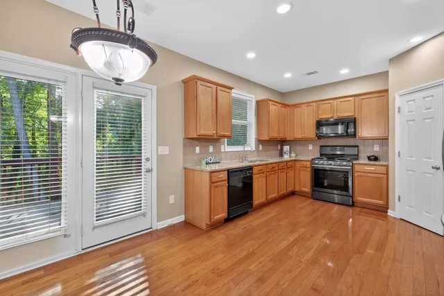 a kitchen with granite countertop a stove a sink dishwasher a refrigerator and a dining table with wooden floor