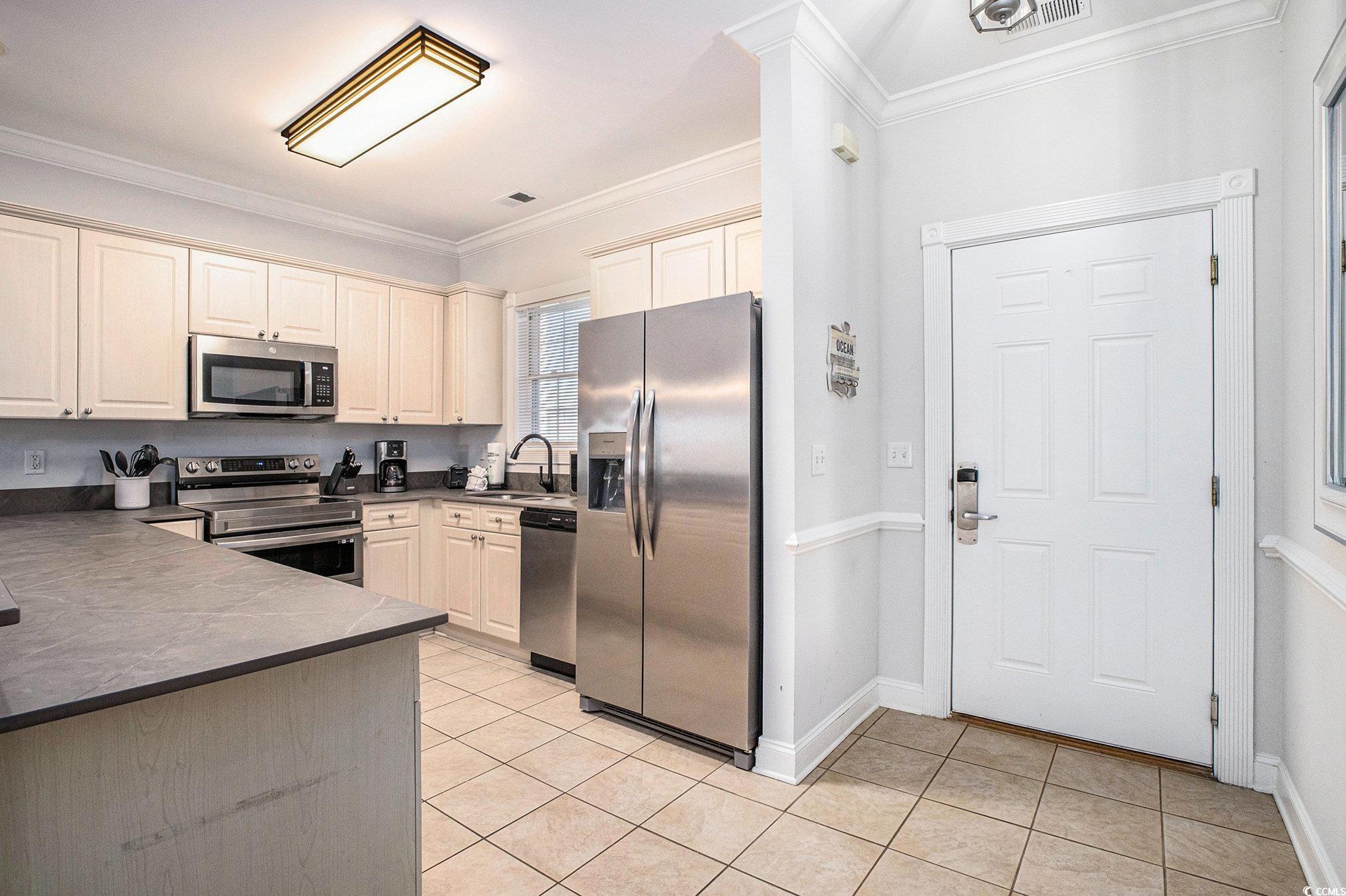4894 Luster Leaf Circle, Unit 303 Myrtle Beach, SC 29577 - Photo 5 of 31 Kitchen with dark countertops, ornamental molding, stainless steel appliances, and light tile patterned flooring