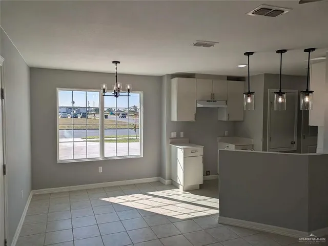 a view of an empty room with kitchen and window