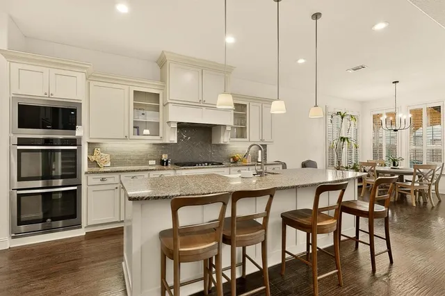 a kitchen with stainless steel appliances granite countertop a stove a sink a microwave a dining table and chairs with wooden floor