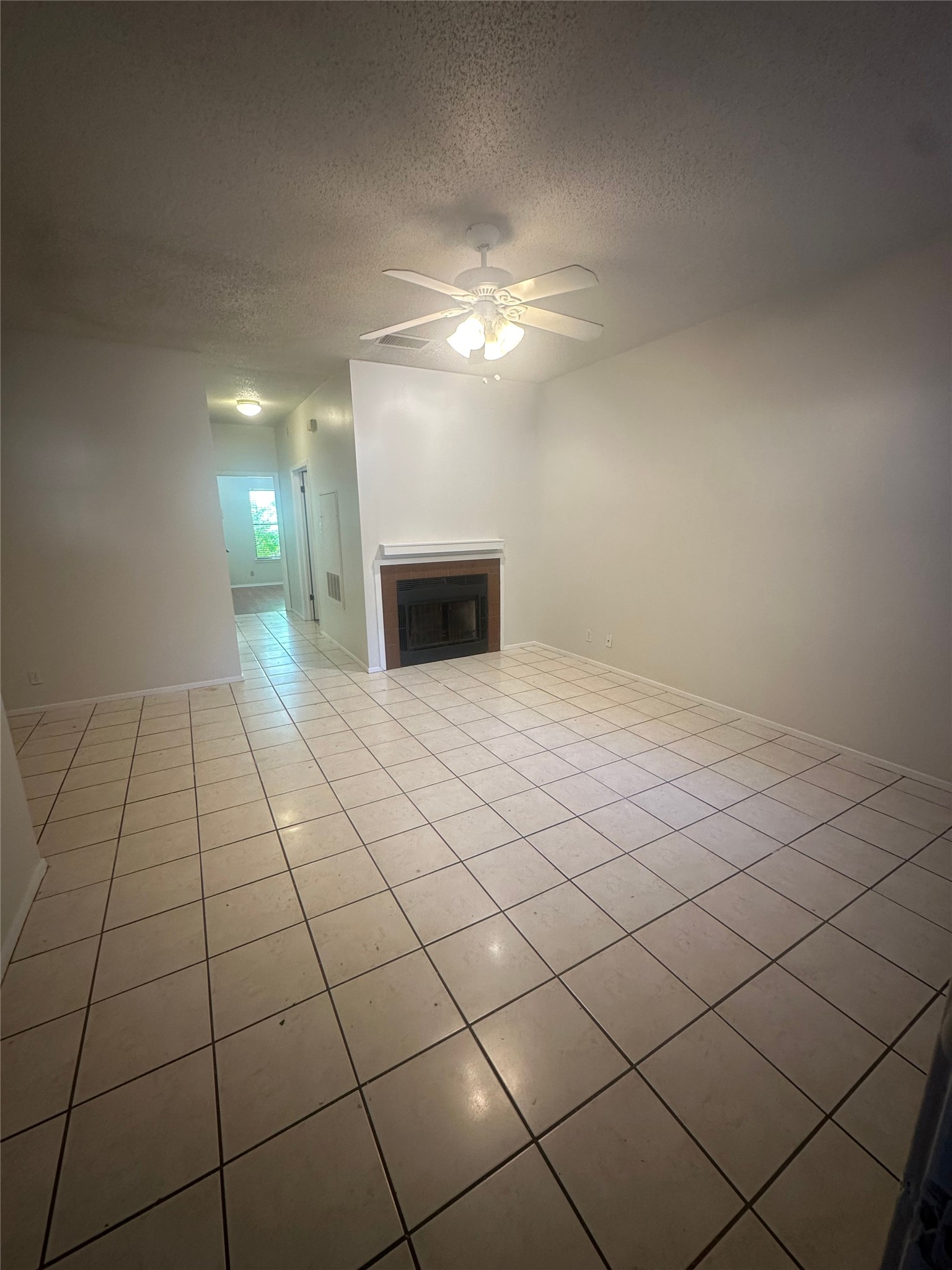 106 East 30th Street, Unit 101 Austin, TX 78705 - Photo 4 of 11 Unfurnished living room featuring a fireplace, a ceiling fan, a textured ceiling, and light tile patterned floors