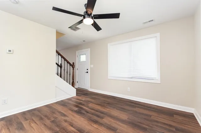 an empty room with wooden floor fan and windows