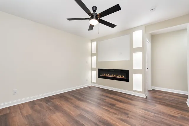 an empty room with wooden floor a ceiling fan a fireplace and a window