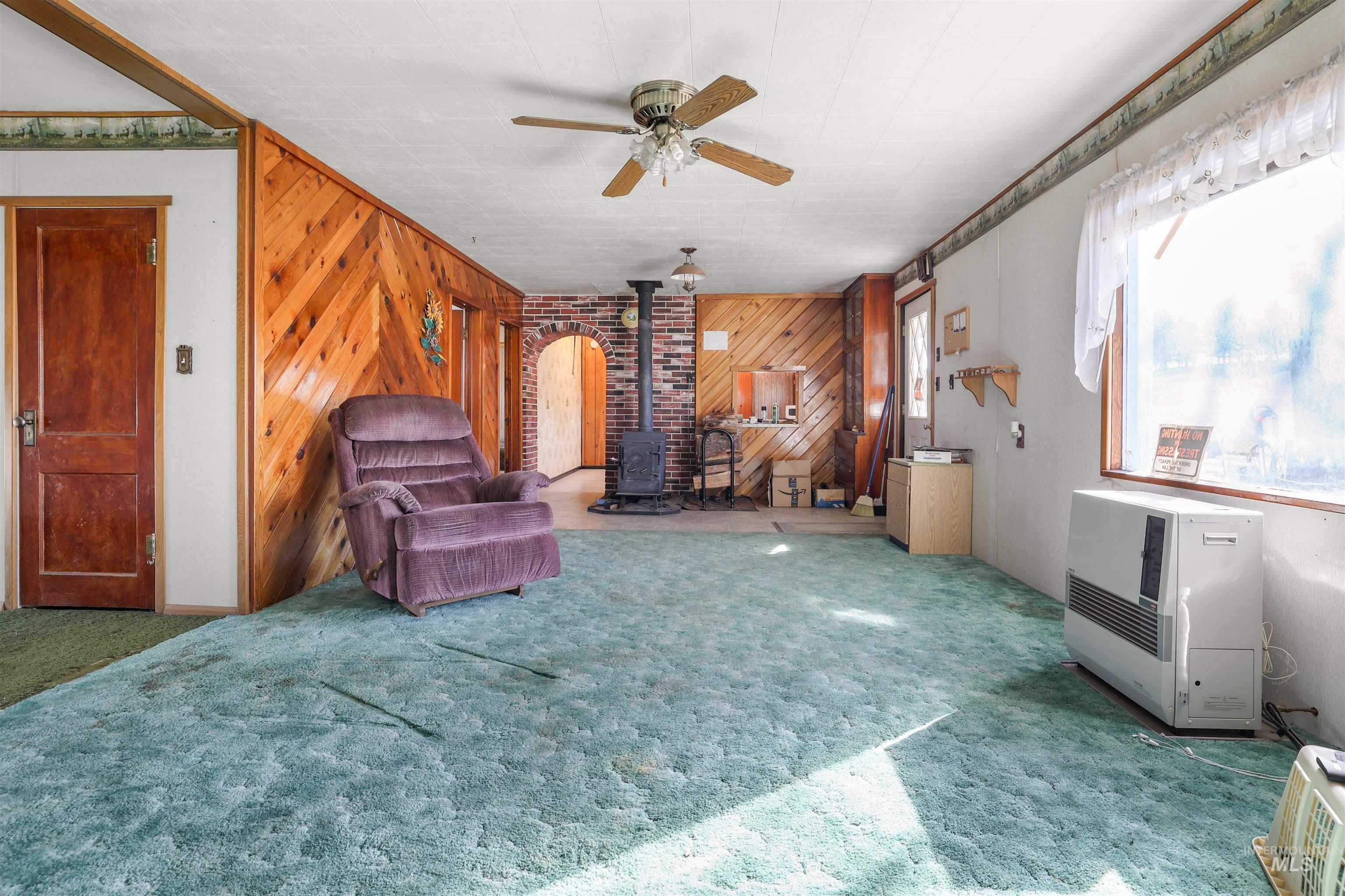 216 Ulmer Road Kooskia, ID 83539 - Photo 27 of 47 Sitting room featuring ceiling fan, a wood stove, wood walls, carpet floors, and heating unit
