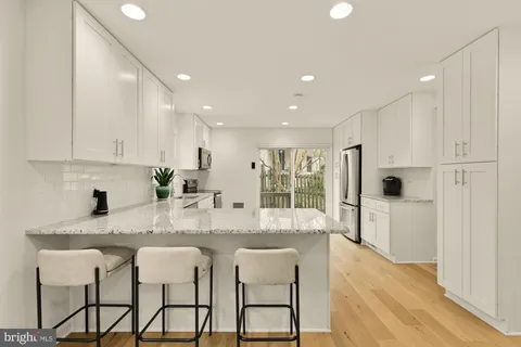 a kitchen with stainless steel appliances granite countertop white cabinets and chairs
