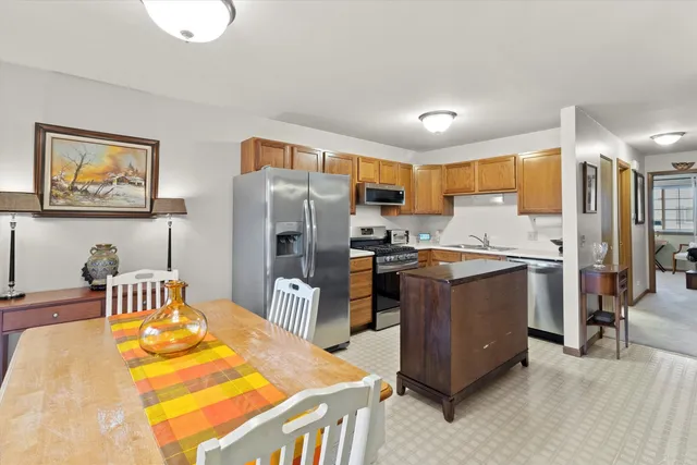 a kitchen with stainless steel appliances granite countertop a refrigerator a stove a sink a dining table and chairs with wooden floor