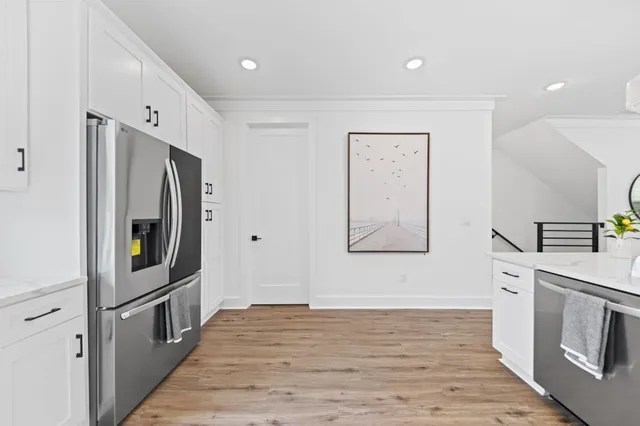 a hallway with wooden floor electronic appliances and white cabinets