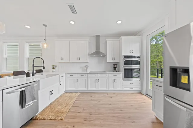 a large kitchen with stainless steel appliances granite countertop a stove top oven a sink a refrigerator and white cabinets with wooden floor