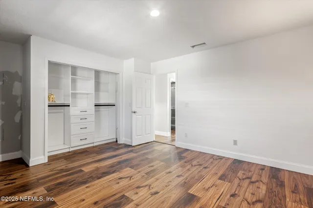 a view of an empty room with wooden floor and closet