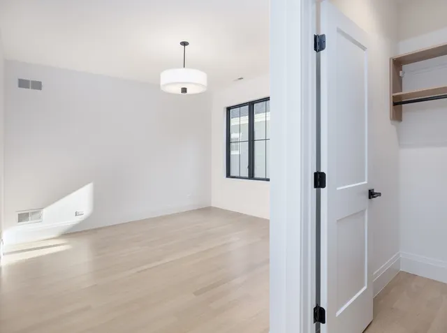 a view of an empty room with wooden floor and kitchen view