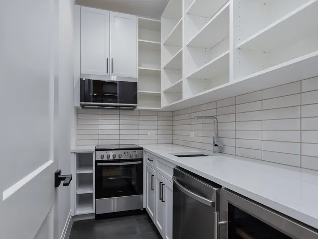 a large kitchen with granite countertop a stove a sink a refrigerator and white cabinets with wooden floor