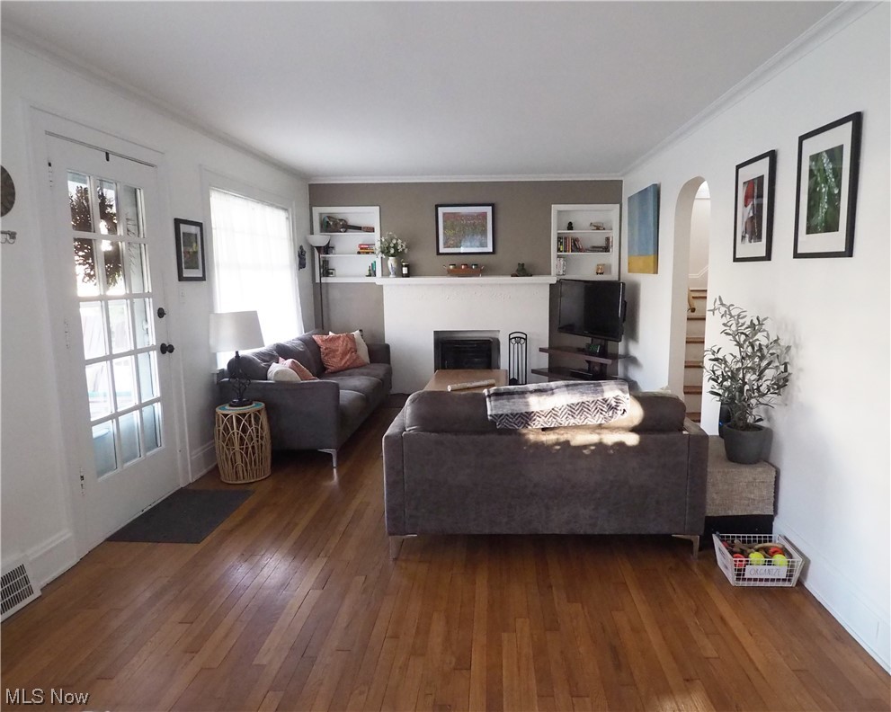 Living room with built in shelves, dark wood-type flooring, plenty of natural light, and crown molding