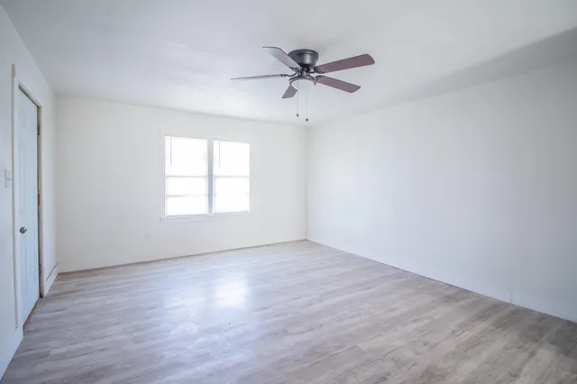 an empty room with wooden floor ceiling fan and windows