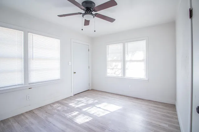 an empty room with wooden floor ceiling fan and windows