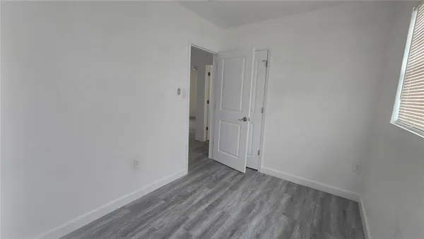 a view of an empty room with wooden floor and window