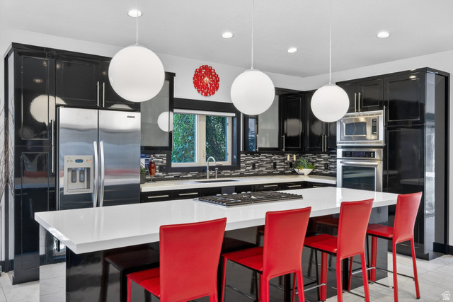 145 Carnesecca Court Mapleton, UT 84664 - Photo 29 of 109 Kitchen with dark cabinetry, a kitchen island, a kitchen breakfast bar, backsplash, and stainless steel appliances