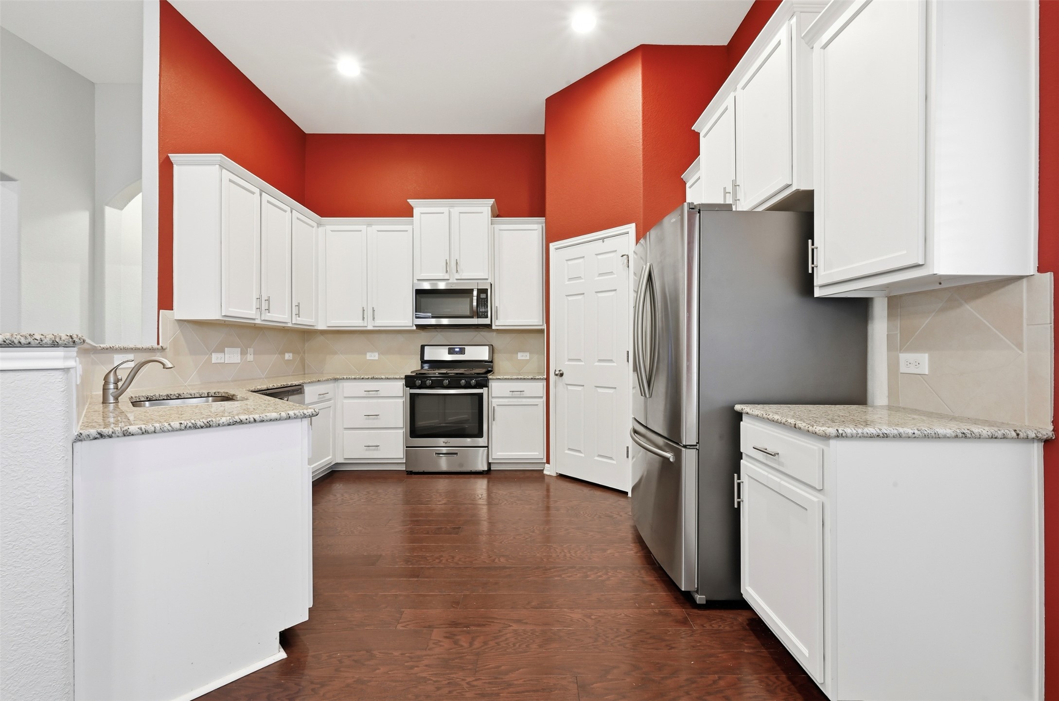 13116 Alans Way Manchaca, TX 78652 - Photo 9 of 25 Spacious kitchen featuring white cabinetry, granite countertops, stainless steel appliances, a tiled backsplash, and wood-finish flooring