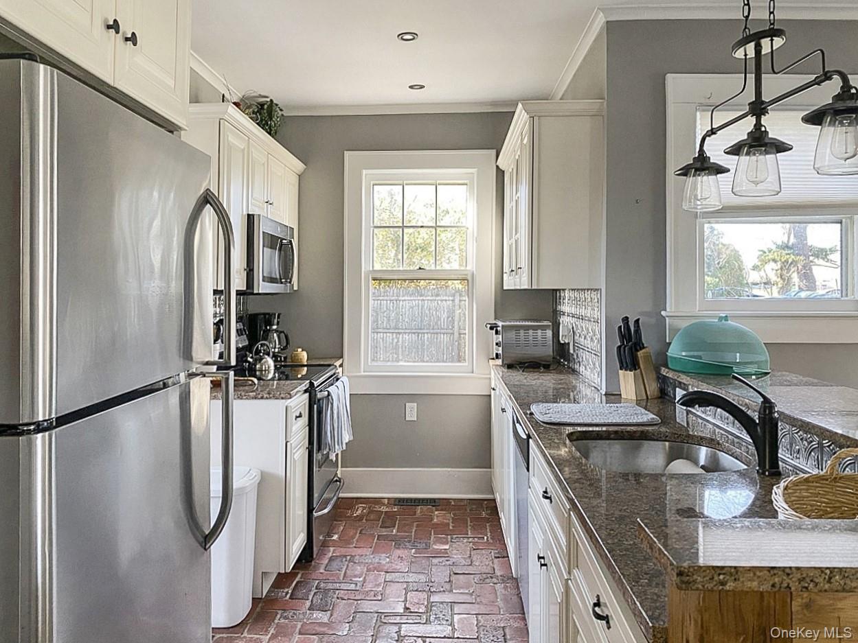 2490 Pike Street Mattituck, NY 11952 - Photo 4 of 15 Kitchen featuring stainless steel appliances, white cabinets, brick floors, dark stone counters, and crown molding