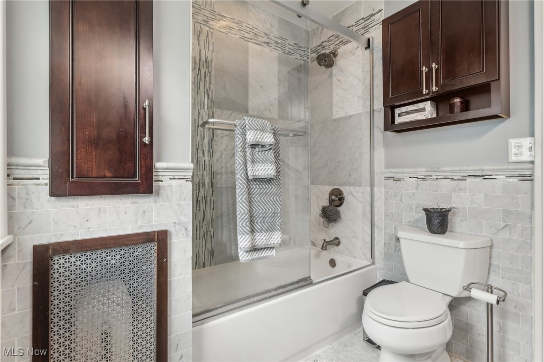 3079 Corydon Road Cleveland, OH 44118 - Photo 30 of 50 Bathroom with tile walls, shower / bath combination with glass door, toilet, and wainscoting