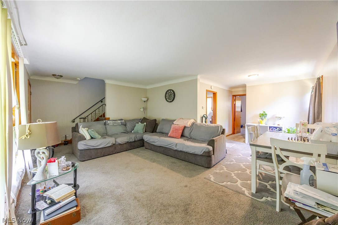 3825 Mayfield Road Cleveland Heights, OH 44121 - Photo 6 of 27 Open-concept living area featuring a neutral color palette, natural light from a prominent window, staircase with dark handrail, and carpeted flooring extending into an adjacent dining space