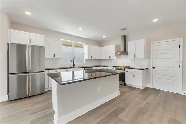 a large kitchen with stainless steel appliances granite countertop a stove a sink a refrigerator and white cabinets with wooden floor