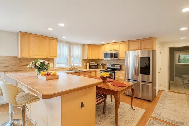 a kitchen with stainless steel appliances granite countertop a refrigerator a stove a sink a dining table and chairs with wooden floor