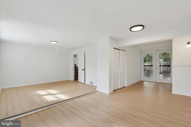 an empty room with wooden floor and way to kitchen