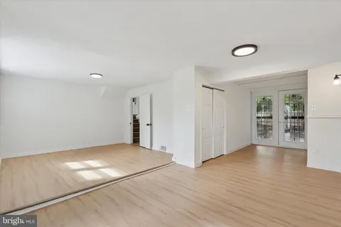 an empty room with wooden floor and way to kitchen