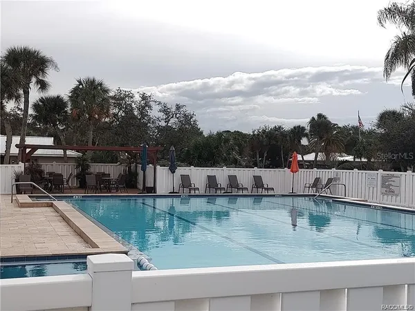 a view of a swimming pool that has lawn chairs and a dining table under an umbrella