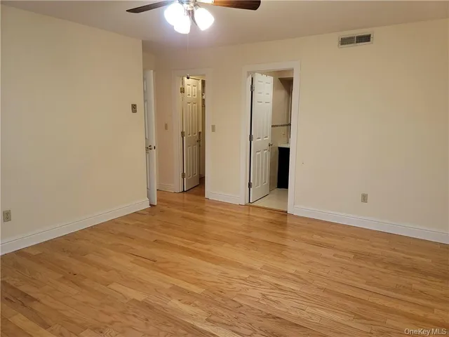 a view of an empty room with wooden floor and chandelier fan