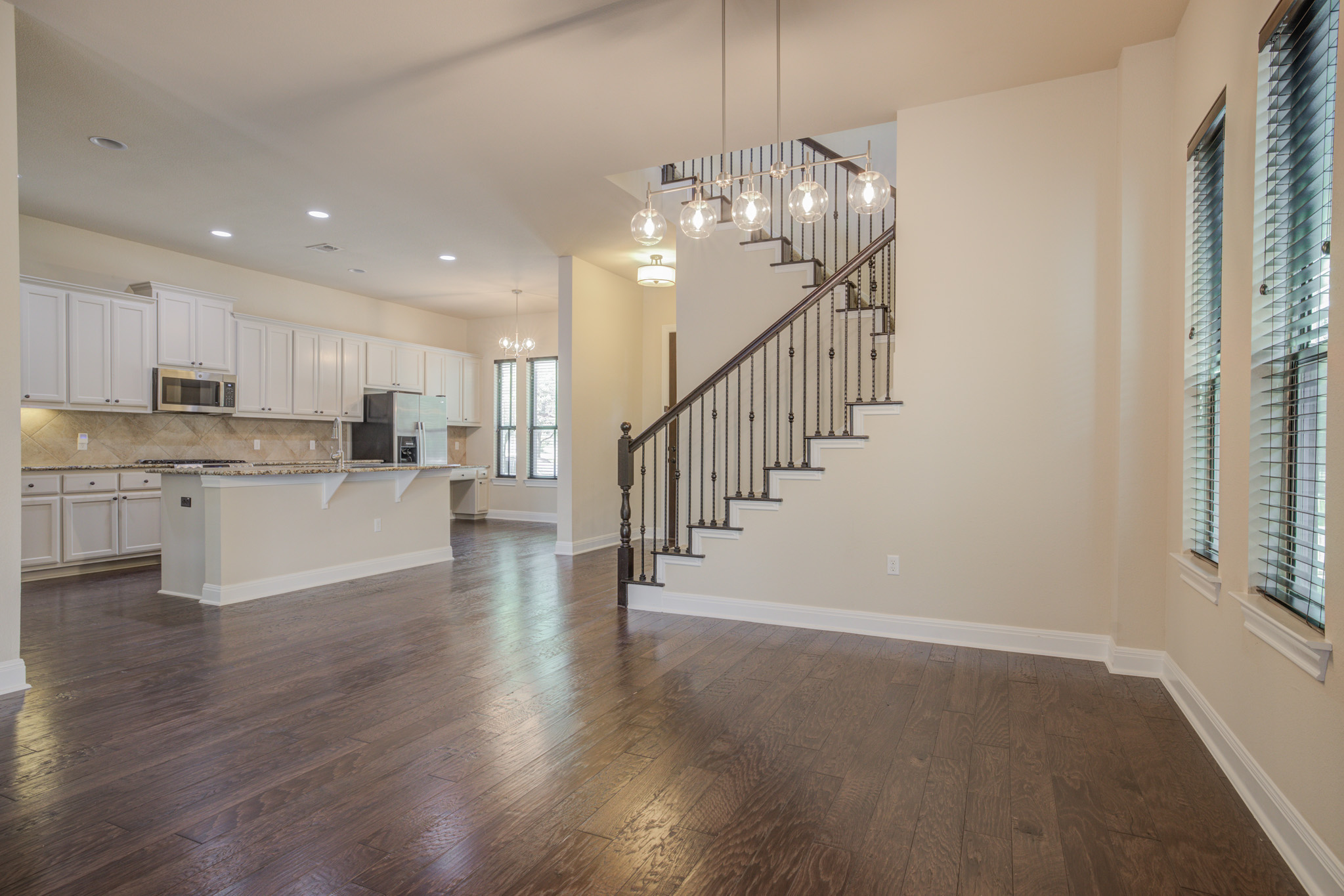 4524 Berkman Drive Austin, TX 78723 - Photo 15 of 38 Expansive main level featuring wood-finish flooring, a modern staircase with wrought iron balusters, a contemporary multi-bulb pendant light fixture, and a kitchen with white cabinetry and a central island