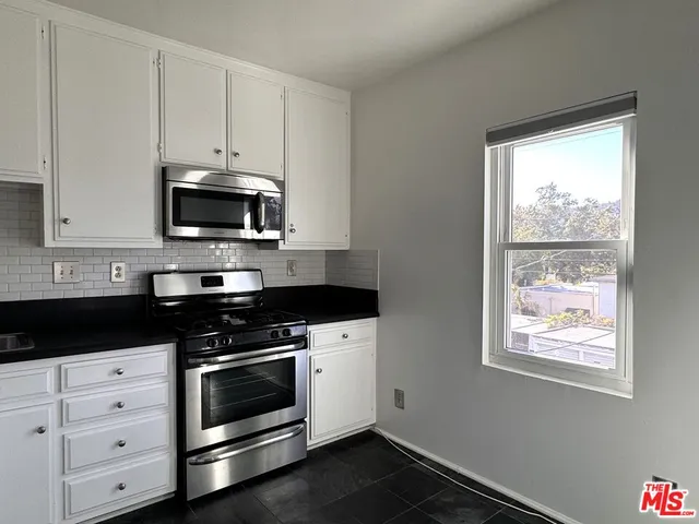 a kitchen with white cabinets appliances and a window