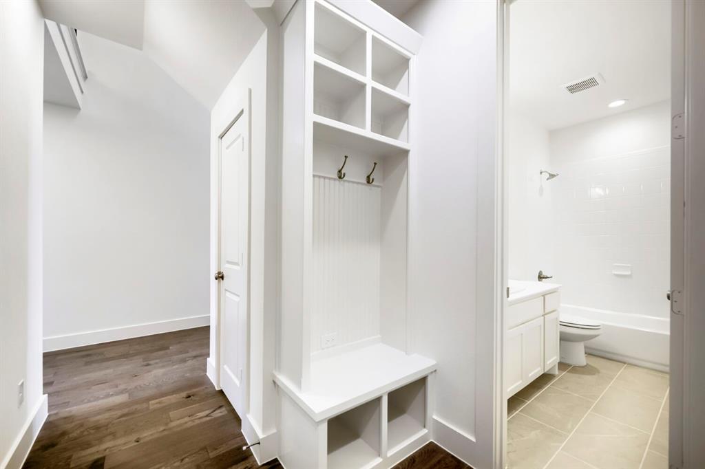 11548 Wulstone Road Haslet, TX 76052 - Photo 19 of 26 Hallway featuring wood-finish flooring, a built-in storage bench with coat hooks and cubbies, a paneled door, and a full bathroom with a tiled floor, white vanity, and tub with subway tile surround