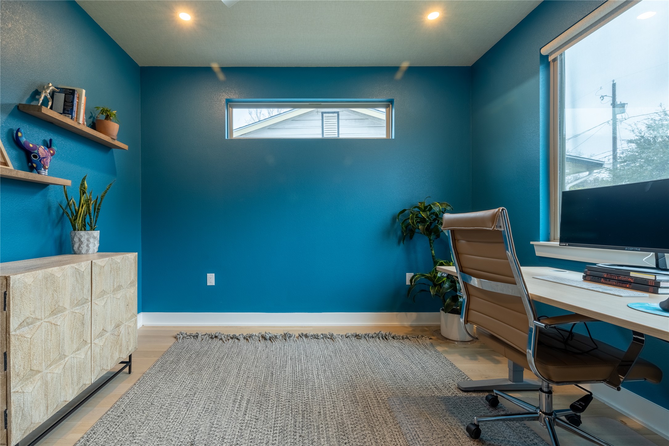 2710 Zaragosa Street, Unit A Austin, TX 78702 - Photo 6 of 29 Blue Suite (Bedroom 1) - Bold blue accent wall sets the tone in this versatile large bedroom or home office — a work-from-home space with built-in shelving and abundant natural light.
