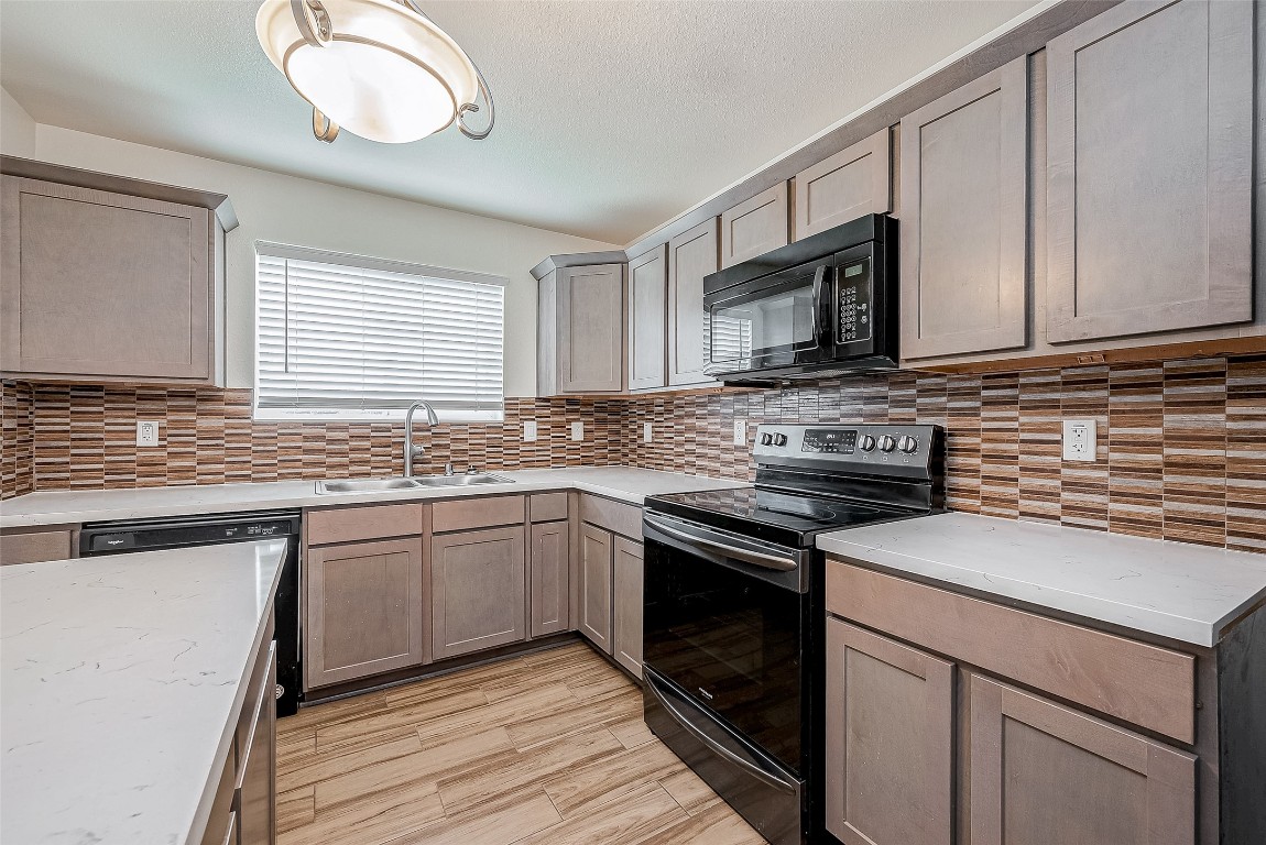 21155 Gosling Road, Unit 15 AB Spring, TX 77388 - Photo 8 of 30 Spacious kitchen with modern wooden cabinets, a central island, and sleek appliances. It features a stylish tile backsplash and ample natural light from a large window.