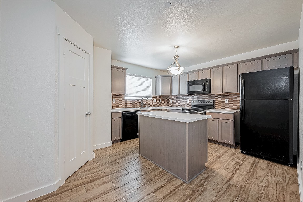 21155 Gosling Road, Unit 15 AB Spring, TX 77388 - Photo 10 of 30 Modern kitchen with wood cabinets, a central island, and stylish tile backsplash. Features a black stove, microwave, and fridge. Adjacent hallway leads to additional rooms.