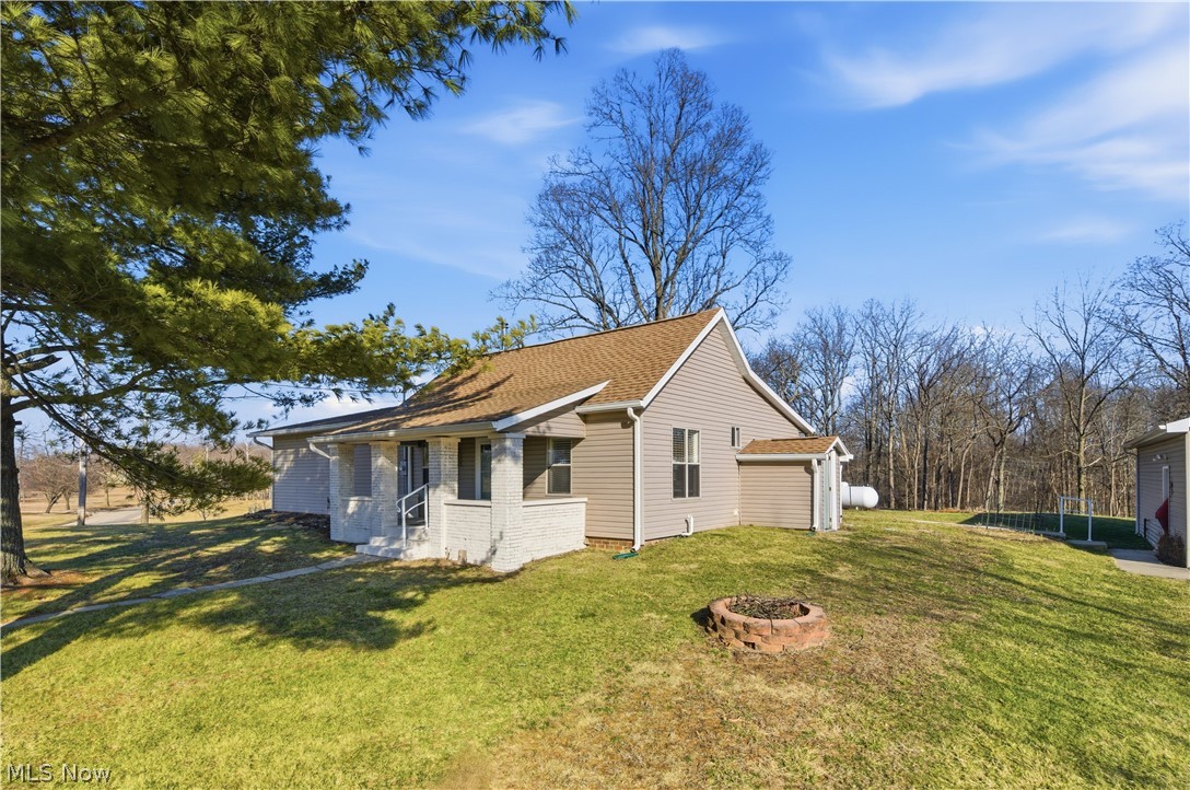 52450 Tower Road Cumberland, OH 43732 - Photo 27 of 41 View of side of home featuring a lawn, a shingled roof, brick siding, and a fire pit