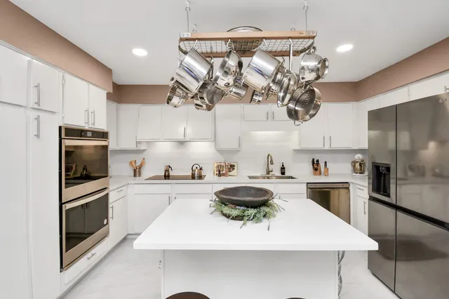 a kitchen with stainless steel appliances a sink a stove a refrigerator cabinets and chairs