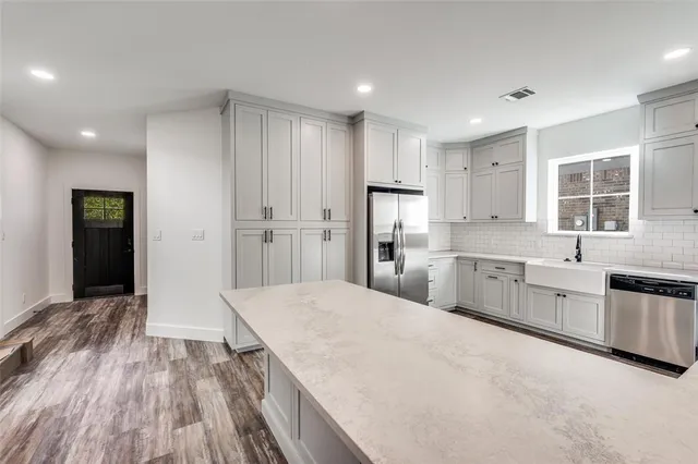 a large kitchen with a refrigerator a sink dishwasher a stove and white cabinets with wooden floor