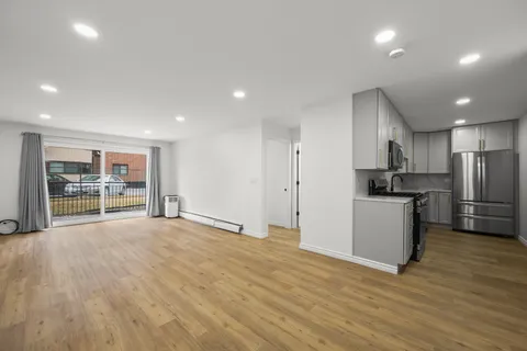 a view of an empty room with wooden floor and a kitchen